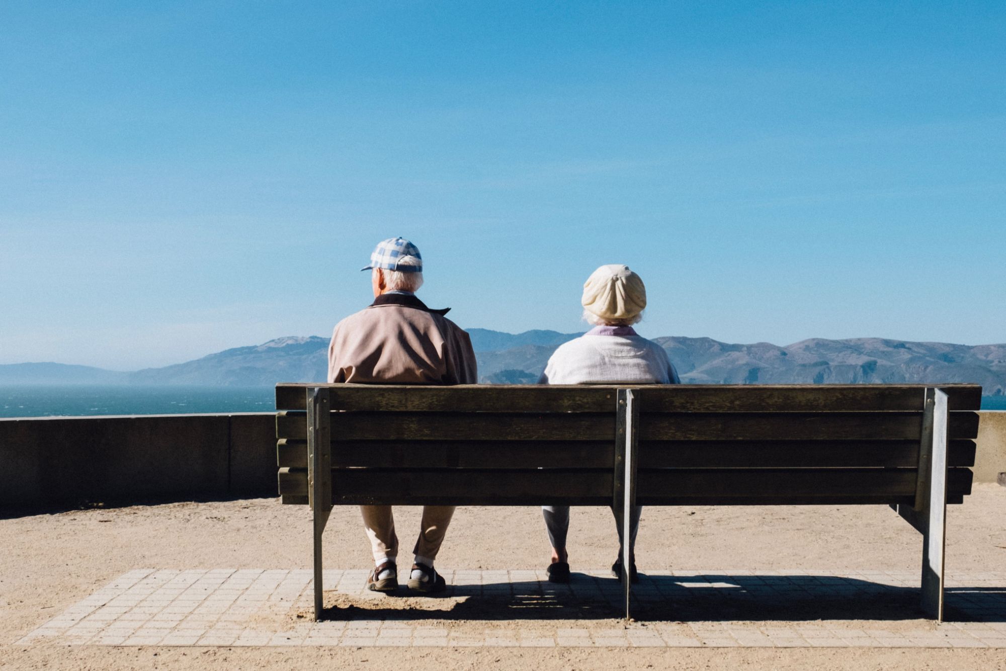Et eldre par som sitter på en benk og ser ut på utsikten over fjell 